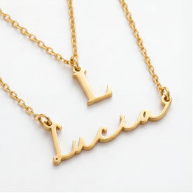 Gold-tone layered necklaces on a white background, featuring a small initial pendant 'L', and a script nameplate reading 'Lucia'.