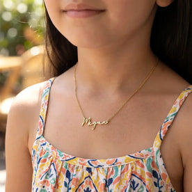 Child wearing gold 'Megan'name necklace on summers day - Anna font