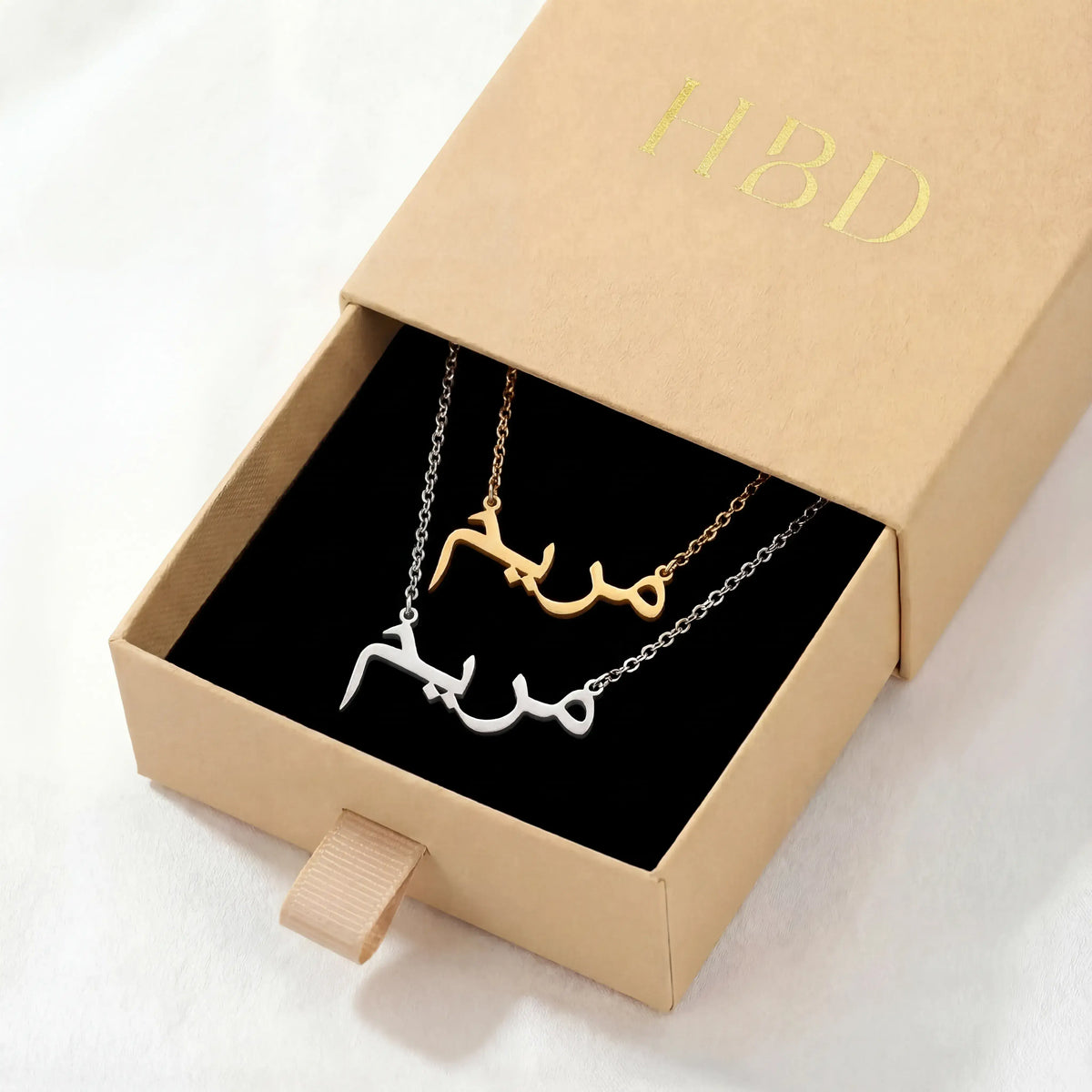 Gold and silver Arabic name necklaces presented in an open beige gift box