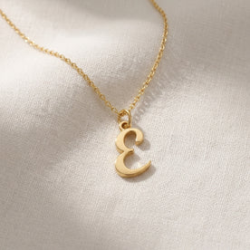 Personalised gold initial necklace with the letter E in the Bella style, laid flat on linen, showing the whole necklace.