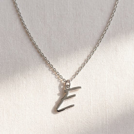 Personalised silver initial necklace with the letter E in the Eva style, laid flat on linen, showing the whole necklace.