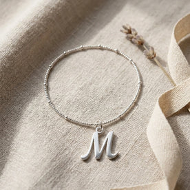 Personalised silver initial bracelet with the letter M in the Bella style, styled on linen with dried flowers.