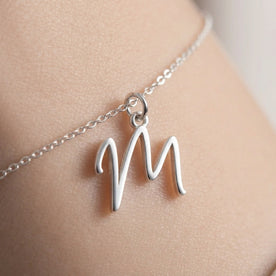 Personalised silver initial bracelet with the letter M in the Zara style, close up, showing the polished cut edge and the thickness of the metal.
