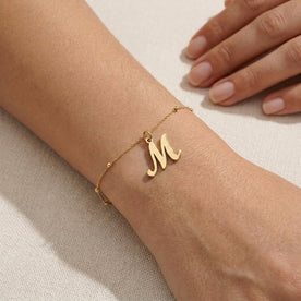 Personalised gold initial bracelet with the letter M in the Eva style, worn on the wrist.