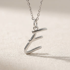 Personalised silver initial necklace with the letter E in the Eva style, close up, showing the polished cut edge and the thickness of the metal.